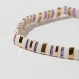 Pulsera elástica con cuentas rectangulares de color blanco, lila y dorado.