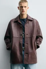 Cazadora de hombre de corte relajado, confeccionada en piel con textura irregular color marrón oscuro (vino/borgoña). Presenta cuello solapa, manga larga con puño abotonado, bolsillos de vivo en cadera, bolsillo interior y cierre frontal con botonadura.