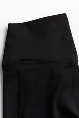 Calzas deportivas negras de tiro alto con bolsillos laterales, confeccionadas en tejido funcional DryMove™ que absorbe la humedad.