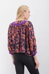 Camisa de corte amplio con estampado animal print en tonos naranja, marrón y violeta, con escote en V con lazos para atar y mangas 3/4 abullonadas.