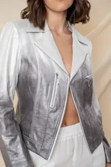 Chaqueta corta de cuero ecológico con diseño degradado de blanco a gris. Tiene cuello tipo solapa, cierre frontal asimétrico con broche y bolsillos con cierre.