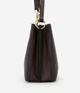 Bolso mediano color marrón oscuro, con doble asa corta y correa larga extraíble. Presenta textura símil cuero y detalle de aro dorado en el frente.