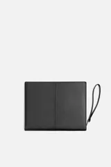 Bolso tipo sobre negro de cuero, con costura central y asa de mano. Cierre con cremallera y compartimentos interiores.