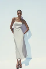 Vestido midi de satén color gris claro, con escote recto, tirantes finos regulables, cuerpo tipo pañuelo con terminación en pico, espalda descubierta con lazo y cierre lateral con cremallera oculta.