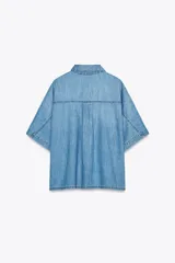 Camisa de denim celeste con cuello solapa, manga corta, bolsillo de parche en el pecho, bajo con aberturas laterales y cierre frontal con botones.