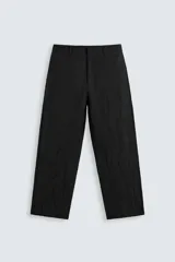 Pantalón negro de corte relajado (relaxed fit) con textura arrugada, tiro medio, bolsillos laterales y bolsillos traseros de vivo. Cierre frontal con cremallera y gancho metálico.