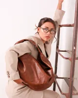 Bolso marrón oscuro de cuero sintético con forma ovalada y asa corta.