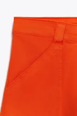 Pantalón de tiro alto color naranja, corte wide leg y largo hasta el tobillo. Tiene bolsillos de parche delanteros y cierre frontal con cremallera y botón.