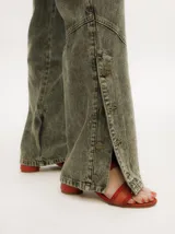 Pantalón de denim verde oliva con efecto gastado, corte recto, tiro medio y botones metálicos en el lateral inferior.