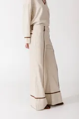 Pantalón de vestir color manteca, de corte recto y tiro alto, con detalle de ribetes marrones en los laterales.