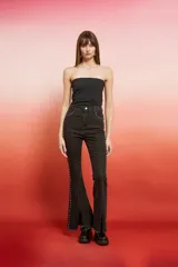 Pantalón de jean de tiro alto, color marrón oscuro con efecto lavado o desgastado, corte flare y tajo en el bajo. Presenta tachas doradas a lo largo de las costuras laterales.