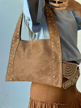 Bolso tipo tote de gamuza color camel con tachas doradas en las tiras y laterales.