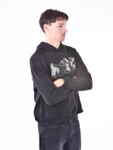 Buzo hoodie negro con cordones ajustables y bolsillo tipo canguro. Estampado frontal con diseño de montañas y texto 'Restless. Explore More'.
