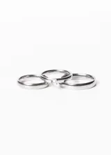 Set de tres anillos dorados, dos alianzas lisas y un cintillo con una piedra engarzada, presentados en un estuche blanco.