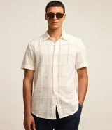 Camisa de manga corta color crema con textura cuadriculada con lesie, cuello inglés y abotonado delantero.