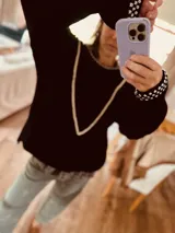 Sweater color crudo con mangas largas color verde oliva. Presenta cuello redondo y detalle de bordado con pompones en forma de V en el frente.