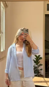 Camisa celeste a rayas verticales blancas, de lino, con cuello camisero y mangas largas con puños abotonados.