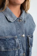 Campera de denim marrón con efecto degradado, corte boxy, cuello camisero, cierre frontal con botones metálicos, mangas largas con puños abotonados, dos bolsillos frontales con solapa y parche con logo en el frente.