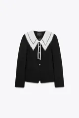 Blazer negro de cuello redondo y manga larga con hombreras. Incluye cuello desmontable blanco con detalle de puntilla. Cierre frontal con botones.
