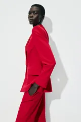 Blazer roja de corte recto, con cuello smoking de satén negro, mangas largas con hombreras, bolsillos frontales con solapa y cierre frontal con un botón.