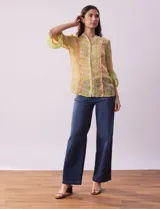 Blusa de gasa estampada con flores amarillas y verdes, marca Alex & Lili. Tiene cuello mao, mangas 3/4 acampanadas y cierre frontal con botones. Presenta volados verticales color naranja en el frente y en las mangas.