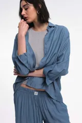 Camisa color marrón de corte holgado, con cuello clásico, mangas largas con puños abotonados y cierre frontal con botones. 