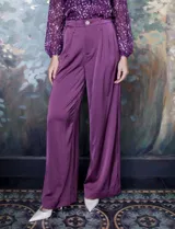 Pantalón palazzo de tiro alto color violeta, de satén. Tiene pretina delantera con pasadores, botón y cierre, pretina trasera elastizada y bolsillos verticales delanteros.