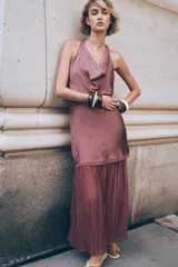 Vestido midi color lila, de cuello halter y sin mangas. La parte superior es de tejido arrugado y la falda es plisada. Tiene abertura en la espalda con cierre de botones ocultos.