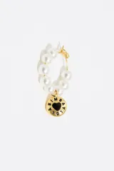 Aros tipo argolla dorados con perlas blancas y dije colgante con logo de la marca y corazón negro.
