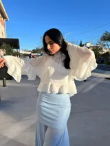 Blusa color blanco hueso, de cuello alto con volados, mangas largas acampanadas con volados y corte crop.