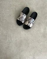 Sandalias chatas color beige con base negra y detalle de bordado blanco en la tira superior.