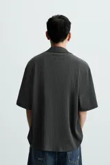 Camisa de manga corta con cuello bowling y calce relajado. Presenta un tejido con textura estructurada y efecto lavado, con cierre frontal de botones al tono.