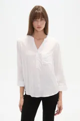 Blusa de manga tres cuartos color crema con estampado floral en azul. Presenta cuello mao con abertura en V y un bolsillo de parche en el pecho.