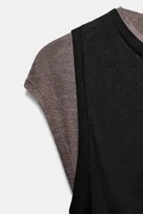 Top de manga caída, con efecto de doble capa. La capa exterior es negra y ajustada, mientras que la capa interior, visible en mangas y cuello, es de color marrón topo.