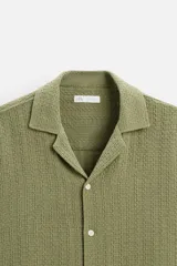 Camisa verde oliva de manga corta con cuello bowling, corte relaxed fit y cierre frontal con botones.