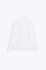 Camisa oversize de algodón blanco, con cuello solapa, manga larga con puños y bajo asimétrico redondeado.