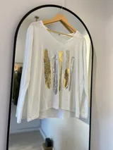 Remera blanca de manga larga con escote en pico y estampa de pinceladas doradas y plateadas en el frente.