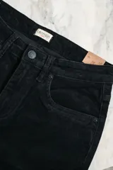 Pantalón de pana negro, tiro medio, corte ajustado hasta la rodilla y acampanado en la parte inferior, con terminación desflecada.