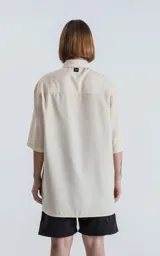 Camisa de manga corta color off-white, con cuello camisero y botones frontales marrones. Corte holgado.