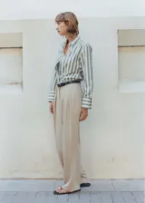 Pantalón color beige de corte wide leg, tiro medio, con trabillas, cierre frontal con botón, gancho y cremallera, detalle de pinzas y diseño largo.