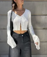 Saco corto de tejido de punto color blanco, con mangas largas y anchas con volados en los puños, y cierre frontal con botones.