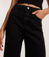 Pantalón negro de sarga con corte años 90, tiro alto, pierna recta y strass aplicados en la parte delantera.
