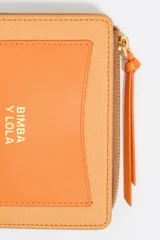 Monedero negro de piel con estructura rígida, logo metálico dorado, tirador de cordón y acabados metálicos dorados. Tarjetero interior, cierre con botón de presión e interior con logo grabado. Confeccionada en 100% poliéster reciclado y 100% poliuretano de producción responsable.