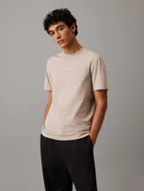 Remera color beige de corte recto, con cuello redondo y mangas cortas. Presenta un logo de Calvin Klein en el pecho.