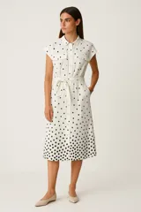 Vestido midi camisero color crudo con estampado de lunares negros, cuello camisero, manga corta, bolsillos laterales y cinturón de lazo.