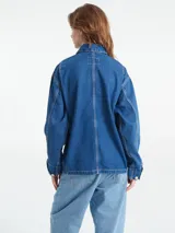 Campera de jean celeste claro, estilo abrigo de trabajo, con cuatro bolsillos delanteros, cierre de botones metálicos grabados con el logo de Carhartt y etiqueta con logo en el bolsillo del pecho.