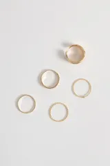 Set de anillos dorados con diferentes diseños, incluyendo un anillo ancho con textura, un anillo con corazones calados, un anillo liso, un anillo trenzado y un anillo con una pequeña piedra.