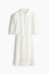 Vestido corto blanco de crepé con secciones de broderie, cuello camisero, botones ocultos, mangas cortas abullonadas, cinturón extraíble y ribete festoneado.