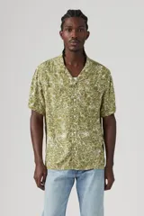 Camisa de manga corta color verde oliva con estampado floral blanco, cuello tipo camp y bolsillo en el pecho.