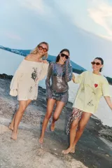 Sweater tejido color crema con cuello amplio que deja un hombro al descubierto. Presenta un estampado con dibujos de estilo boceto en negro y rojo, y detalles de roturas en las mangas.